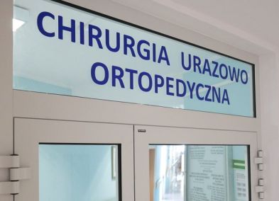 Zdjęcie przedstawia górny fragment drzwi wiodących na szpitalny oddział i widniejący nad nimi napis: Chirurgia Urazowo Ortopedyczna. 